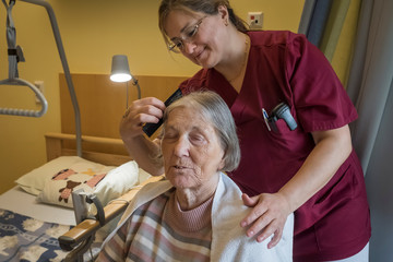 Eine Fachpflegerin in weinroter Funktionskleidung kämmt das Haar einer Hospizgästin an deren Pflegebett in einem Gästezimmer des Diakonie Hospiz Volksdorf in Hamburg-Volksdorf. 
