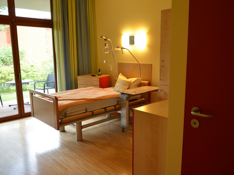 Blick in ein Gästezimmer mit Bett und Blick auf Terrasse - Diakonie Hospiz Volksdorf