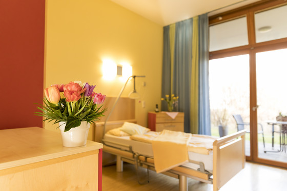 Das Bild zeigt ein Zimmer im Hospiz. Darin steht ein Bett an einem großen Fenster. Das Bild zeigt ein Zimmer im Hospiz. Darin steht ein Bett an einem großen Fenster.