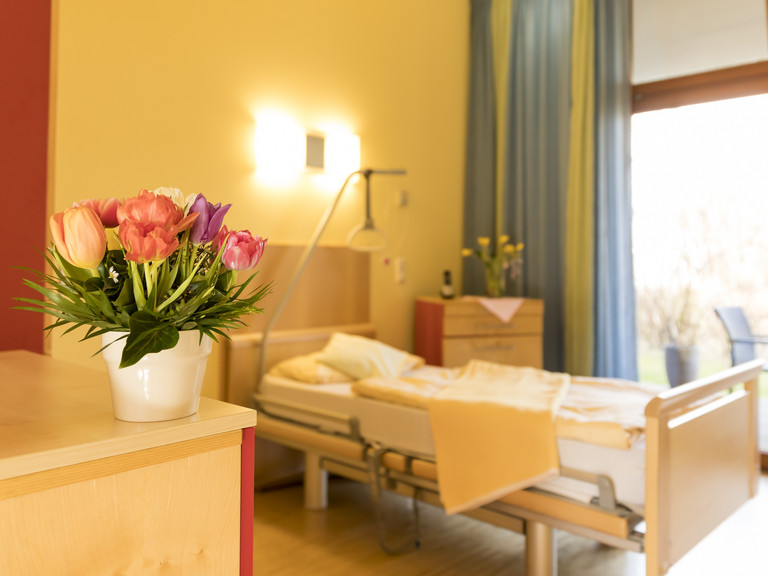 Blick in ein helles Gästezimmer mit Bett und Blumenstrauß im Diakonie Hospiz Volksdorf Blick in ein helles Gästezimmer mit Bett und Blumenstrauß im Diakonie Hospiz Volksdorf